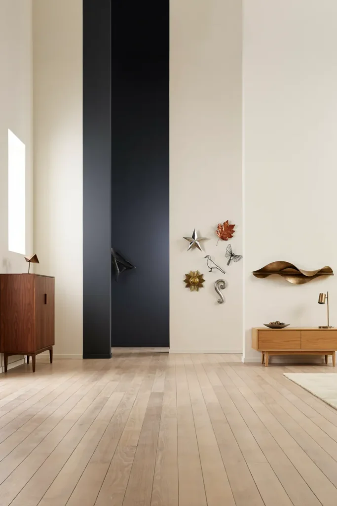Minimalist room with a white wall, a dark vertical panel, and a sculptural metal wall piece