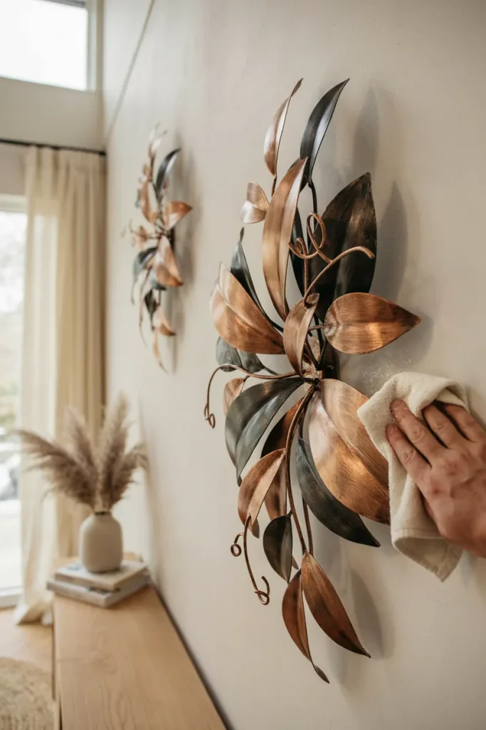 Leaf-shaped metal wall sculpture in warm copper tones on a light wall beside a potted plant
